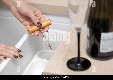 femme tient un tire-bouchon dans sa main pour ouvrir une bouteille de vin. la main d'une femme prend un tire-bouchon dans un tiroir de cuisine. alcoolisme féminin. faible profondeur Banque D'Images