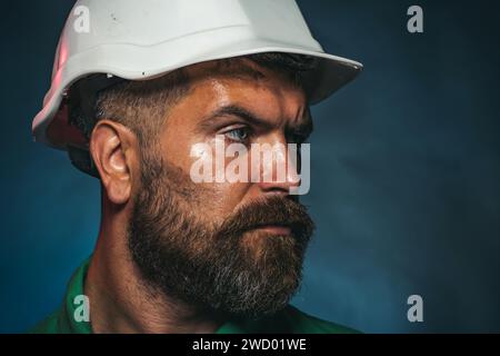 Portrait en gros plan du constructeur masculin dans le casque de construction regardant sur le côté. Ouvrier mécanique ou industriel dans le casque de sécurité regarde loin. Homme barbu sérieux Banque D'Images