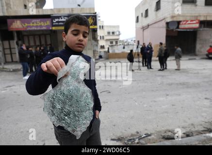 Naplouse. 17 janvier 2024. Un garçon ramasse les débris d’un véhicule bombardé par l’armée israélienne dans la ville de Naplouse en Cisjordanie, le 17 janvier 2024. Au moins sept Palestiniens ont été tués mercredi par des frappes israéliennes en Cisjordanie, ont indiqué des sources médicales et sécuritaires palestiniennes. La Société palestinienne du Croissant-Rouge (SCRP) a rapporté mercredi que l’armée israélienne a bombardé un véhicule palestinien dans la ville de Naplouse, dans le nord de la Cisjordanie, causant la mort de trois Palestiniens, dont deux frères du camp de réfugiés de Balata à Naplouse. Crédit : Ayman Nobani/Xinhua/Alamy Live News Banque D'Images