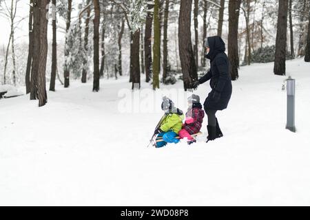 Joyeux petit frère et soeur en vêtements chauds jouant joyeusement avec mère Sledding Banque D'Images