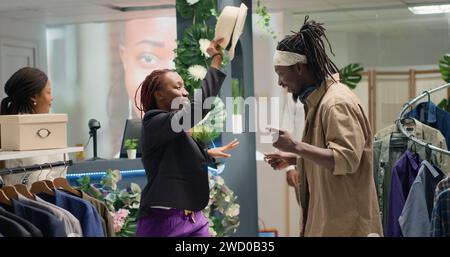 Couple afro-américain étant idiot ensemble dans le magasin de vêtements, être heureux des ventes de promotion. Les clients BIPOC dans la boutique de mode s'amusent, foutent, sont excités par les bas prix Banque D'Images