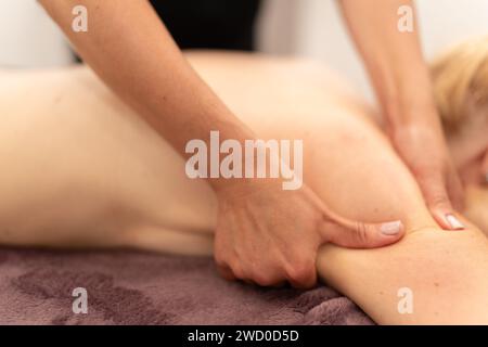 Un massothérapeute qualifié travaille doucement sur l'épaule et le dos d'un client, soulageant la tension et favorisant la relaxation dans une salle de spa paisible. Banque D'Images