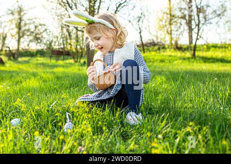 Portrait de petite fille blonde portant des oreilles de lapin souriant dans le jardin. Chasse aux œufs de Pâques Banque D'Images