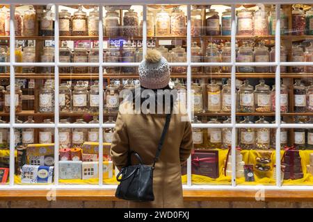 Une femme portant un chapeau en hiver regardant dans la fenêtre de Hamiltons de Broadway, une boutique de confiserie traditionnelle anglaise. Angleterre Banque D'Images