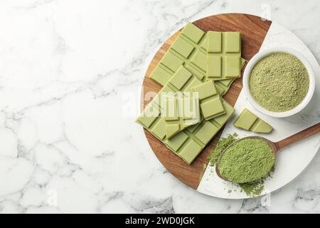 Morceaux de savoureuse barre de chocolat matcha et poudre sur table en marbre blanc, vue de dessus. Espace pour le texte Banque D'Images