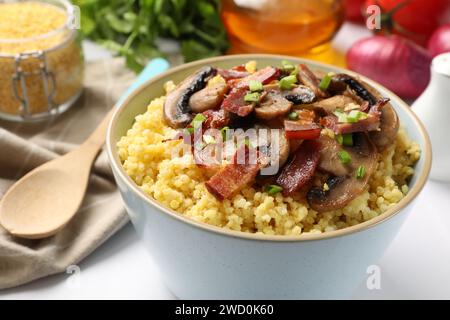 Savoureux porridge de millet avec des champignons, du bacon et de l'oignon vert dans un bol sur une table blanche, gros plan Banque D'Images