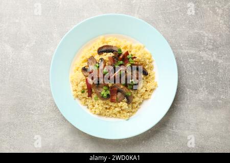 Savoureux porridge de millet avec champignons, bacon et oignon vert sur table texturée grise, vue de dessus Banque D'Images
