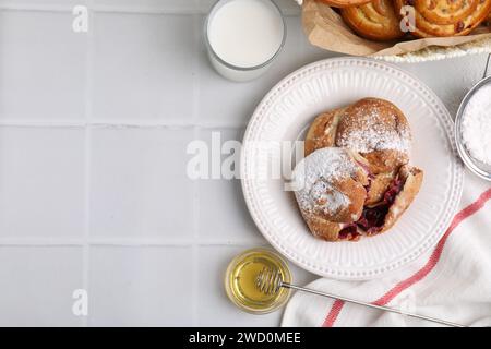 Délicieux rouleaux avec de la poudre de sucre et des baies sur la table carrelée blanche, plat avec espace pour le texte. Petits pains sucrés Banque D'Images