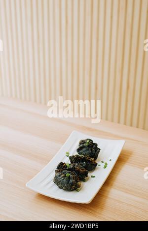 Gyoza frit noir sur une assiette sur une table en bois. Cuisine de rue traditionnelle japonaise. Banque D'Images