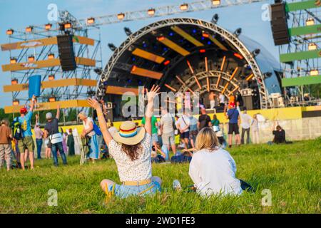 Vue arrière des gens s'amusant à un festival de musique d'été, profitant d'une performance en direct en plein air, avec une femme levant les mains. Banque D'Images
