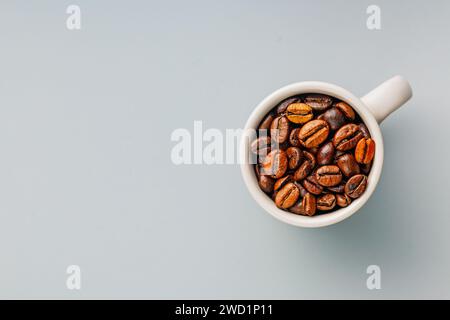 Grains de café torréfiés dans une tasse de café sur le fond gris. Vue de dessus. Banque D'Images
