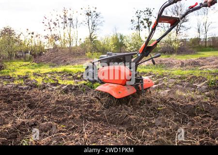 Cultivateur à moteur avec une roue avant relevée et un sillon inséré dans le sol pendant le labourage du champ avant de semer des semences et de planter des semences Banque D'Images