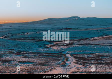 Une belle vue lointaine d'Ingleborough dans le parc national des Yorkshire Dales au coucher du soleil par une journée d'hiver enneigée, avec un ciel clair et net en janvier 2024. Banque D'Images