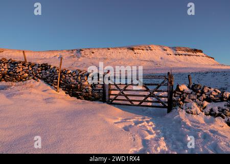 Un mur de pierres sèches avec une porte en bois et Pen-y-ghent en arrière-plan dans le parc national des Yorkshire Dales. Pris en hiver avec de la neige au coucher du soleil. Banque D'Images