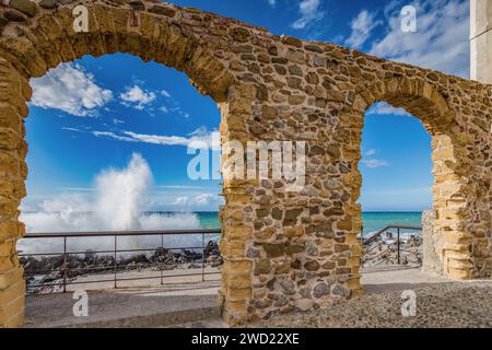 Vagues se brisant sur les rochers vus d'une arche de pierre sur la jetée de Cefalù, Sicile Banque D'Images