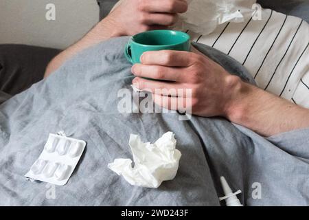 Hanovre, Allemagne. 12 décembre 2023. Un homme est allongé dans son lit avec des mouchoirs, une tasse de thé, un spray nasal et des comprimés (scène mise en scène). Alors que la pandémie de corona diminue, un autre virus est maintenant en hausse. (À dpa 'RKI : nombre croissant de cas de grippe signalés - tous les groupes d'âge touchés') crédit : Philip Dulian/dpa/Alamy Live News Banque D'Images