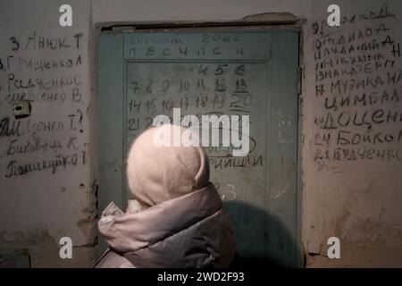 YAHIDNE, UKRAINE - 17 JANVIER 2024 - Une femme fait face à la porte avec le calendrier et le mur avec les noms des personnes qui sont mortes dans le sous-sol de l'école où les occupants russes détenaient plus de 300 résidents, dont 77 enfants, captifs du 3 au 30 mars 2022, Yahidne, région de Tchernihiv, nord de l'Ukraine. Banque D'Images