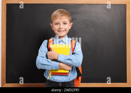 Heureux écolier avec sac à dos et livres près du tableau noir Banque D'Images