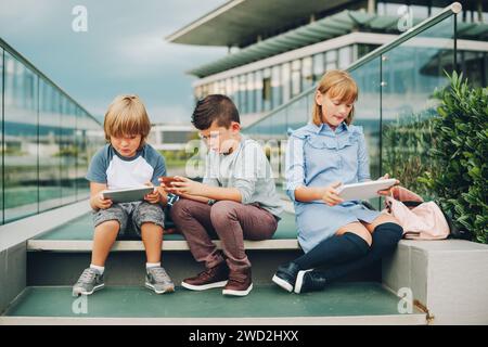 Groupe de 3 enfants drôles jouant avec tablette pc à l'extérieur. Jeunes enfants utilisant des gadgets électroniques Banque D'Images