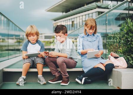 Groupe de 3 enfants drôles jouant avec tablette pc à l'extérieur. Jeunes enfants utilisant des gadgets électroniques Banque D'Images