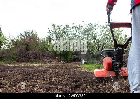 Cultivateur à moteur avec une roue avant relevée et un sillon inséré dans le sol pendant le labourage du champ avant de semer des semences et de planter des semences Banque D'Images