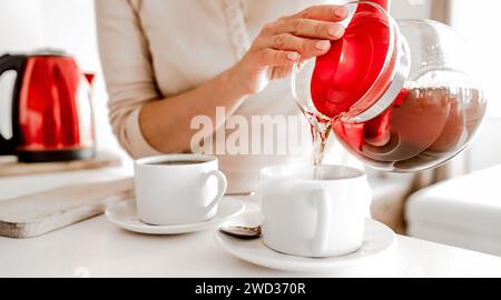 Une fille verse du thé chaud dans des tasses de thé dans la cuisine. Femme préparant une boisson chaude à base de plantes avec une bouilloire et des tasses Banque D'Images