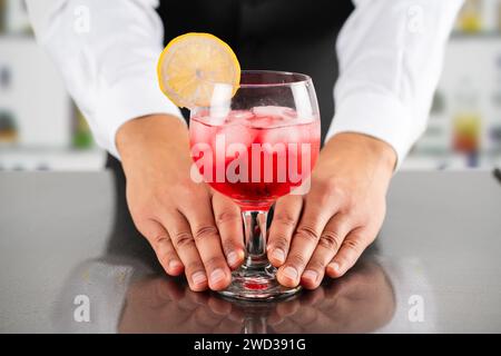 Vue rapprochée d'un verre à cocktail avec de la glace et du citron vert brillant dans les mains d'un barman mâle. arrière-plan flou Banque D'Images