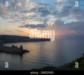 Cala Morell, Minorque, Îles Baléares, Espagne. Vue sur la mer Méditerranée tranquille à la Punta de s'Escullar, coucher de soleil. Banque D'Images
