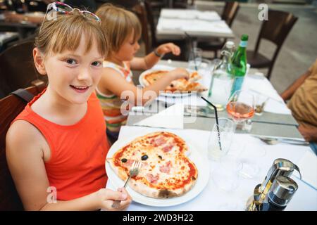 Heureuse petite fille mangeant de la pizza pour enfants dans le restaurant. Menu pour enfants, pizza italienne en forme de coeur Banque D'Images