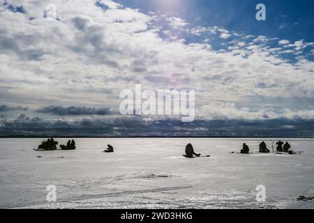 silhouettes de pêcheurs pêchant et motoneige en hiver sur la glace de la rivière sous le ciel nuageux bleu jour de gel Banque D'Images