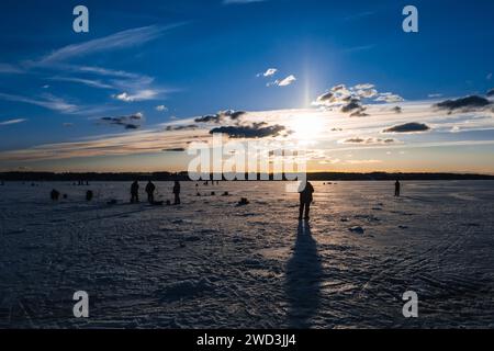 silhouettes de pêcheurs pêchant et vis à glace en hiver sur le lac au lever du soleil le matin Banque D'Images