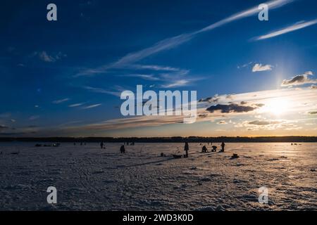 silhouettes de pêcheurs pêchant et vis à glace en hiver sur le lac au lever du soleil le matin Banque D'Images