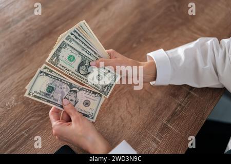 Vue de dessus en gros plan de la réussite du comptage de l'argent féminin. Gros plan d'une femme méconnaissable calculant des dollars en espèces à la maison assis au bureau. Concept de Banque D'Images