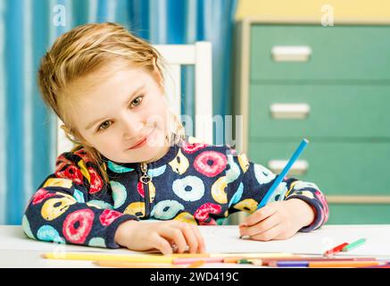 Charmante petite fille blonde aux yeux beauriful attire avec des crayons et regarde l'appareil photo Banque D'Images