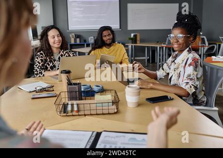 Groupe diversifié de collègues écoutant une femme méconnaissable qui leur parle lors d'une réunion d'affaires Banque D'Images