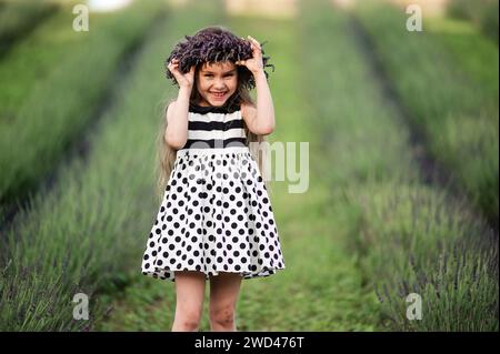 mignonne petite fille souriant et fixant sa couronne qui est tombée de sa tête, marchant dans un champ de lavande. Banque D'Images