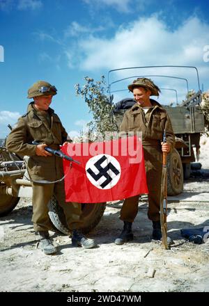 PRÈS DU HAUT MESNIL, FRANCE - 10 août 1944 - deux soldats de l'Armée canadienne hissent un drapeau nazi qu'ils ont capturé dans une carrière au sud de Hautmesnil, France - Banque D'Images