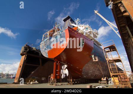 Navire commercial en cale sèche pour entretien. Le navire subit la peinture et les réparations de la coque. Procédé de transport maritime industriel. Les ouvriers remettent en état le bateau Banque D'Images