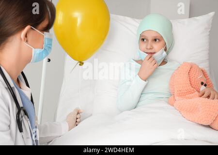 Petite fille après chimiothérapie recevant un ballon bleu du médecin en clinique. Journée internationale contre le cancer chez l'enfant Banque D'Images