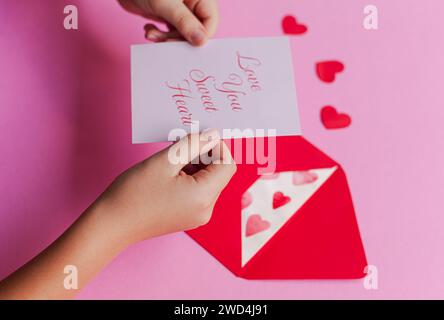 Femme présentant une carte blanche dans une enveloppe rouge vibrante, accompagnée d'un délicat diamant en papier Banque D'Images