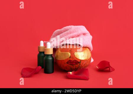 Citrouille avec visage dessiné, taches sous les yeux, sérum et pétales de rose sur fond rouge Banque D'Images