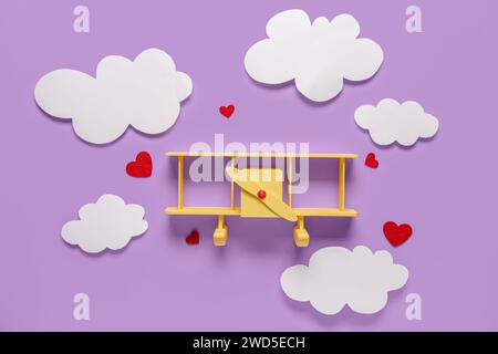 Avion jouet avec des coeurs et des nuages sur fond lilas. Fête de la Saint-Valentin Banque D'Images