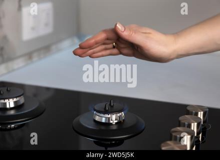 Une femme tient sa main sur une surface de gaz avec le gaz allumé. Banque D'Images
