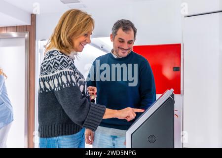 Les patients souriant tout en planifiant des rendez-vous à l'hôpital en utilisant une machine moderne dans le hall Banque D'Images