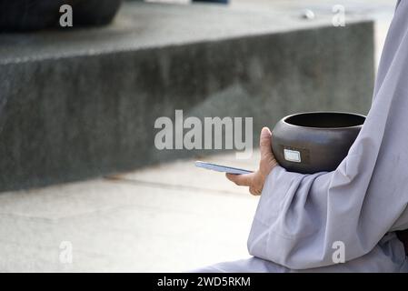 Une main de moine avec un bol d'aumônes et un téléphone moderne. Banque D'Images