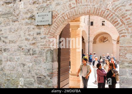 Gubio Ombrie, Italie, mai 12 2011 ; plaque nominative sur le mur à l'entrée tandis que les touristes se promènent dans la cour de la basilique médiévale de Saint Ubaldo. Banque D'Images