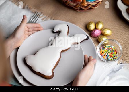 Biscuit en pain d'épice glacé en forme de lapin de Pâques. Mains de l'enfant tenant la plaque avec biscuit Banque D'Images