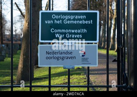 Signe du cimetière des graves de guerre du Commonwealth, avec texte anglais et néerlandais. Derrière la clôture, les pierres tombales Banque D'Images