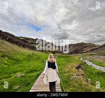 Femme marche le long du chemin à travers les champs d'herbe verte à la cascade Banque D'Images