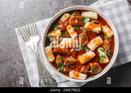 Boulettes de pommes de terre polonaises traditionnelles maison kopytka servies avec du ragoût de viande en gros plan dans une assiette sur la table. Vue de dessus horizontale Banque D'Images